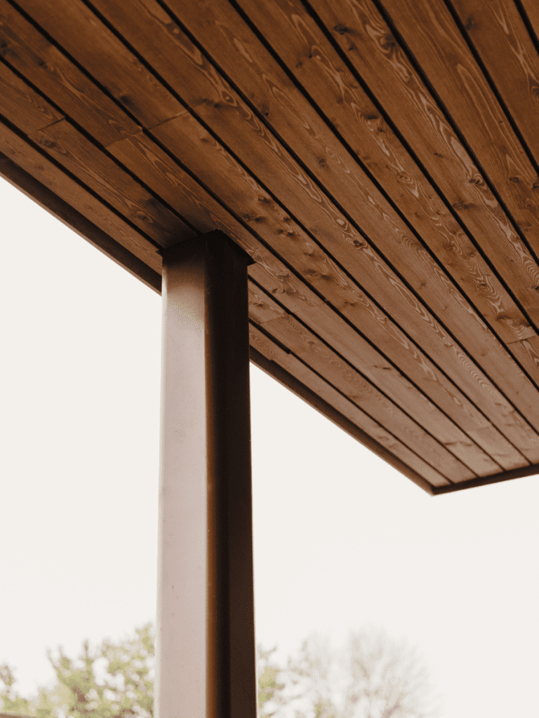 Detail van houten afwerking en stalen paal ter ondersteuning van een overdekt terras.